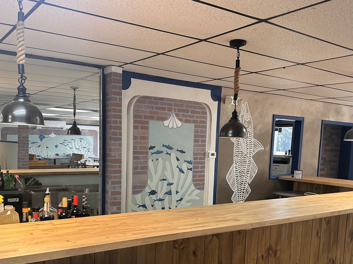 The bar — butcher-block counter, rope pendant lights, stocked shelves and the fish mural behind
